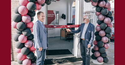 Andrew Tapsell and David Cherry  in front of a balloon arch in front of the Isle of Wight office. David Cherry is cutting the ribbon for the grand opening